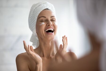 133881637-positive-funny-young-woman-laughing-while-applying-facial-cream-reflecting-in-mirror-happy-attractiv